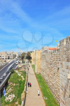 Walk along the walls of ancient Jerusalem. View of the New Jerusalem - the highway with cars, modern buildings and people walking