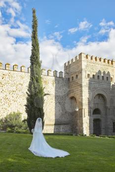 The bride in a magnificent wedding dress with a loop is photographed at walls of ancient city Toledo in Spain