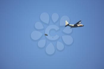  The military plane and a parachute with the parachuter in the dark blue sky above quay of Tel Aviv