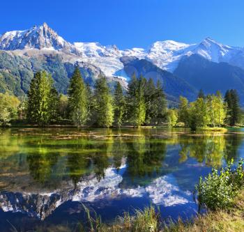 City park in the mountain resort of Chamonix in France. Snowy mountains and evergreen spruce reflected in the lake