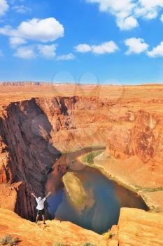 An enthusiastic traveler raised his hands on a steep and dangerous shore of the Colorado River. The well-known river Colorado is picturesquely bent in the Horseshoe.