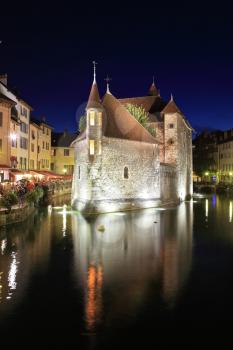 Summer night in the charming medieval town. Old fortress-prison on the island in the middle of the river. Castle illuminated by spotlights and is beautifully reflected in the dark water.