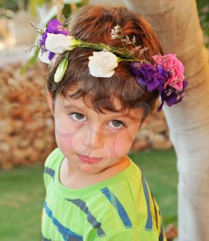 Very beautiful little boy posing in the garden. This holiday - his birthday. He wore a wreath of flowers