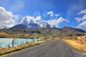 The gravel road along the shore of Lake Pehoe. The National Park Torres del Paine in Chile. In the distance are seen cliffs of Los Cuernos