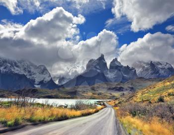  Picturesque clouds piled up in the blue sky. The gravel road goes to the famous cliffs of Los Kuernos. Windy day in the Chilean Patagonia.