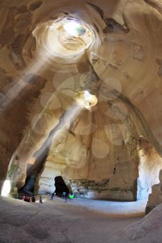Israel National Park. Bell caves of Beit Guvrin. Picturesque clay arches illuminated by the sun from the hole at the top and side entrances