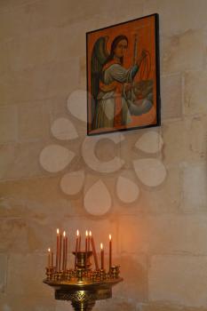 Burning candles in a bronze candlestick. On the wall - a great icon of the archangel with wings