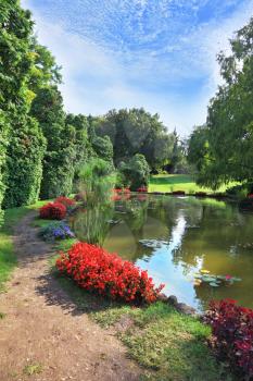 Beautiful park in northern Italy Sigurta. Picturesque bush with red flowers around a circular pond