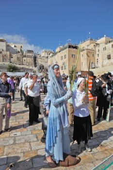 Jerusalem - October 16: The Holy Western Wall of the Temple. A young woman in a very beautiful religious dress smiles and holds the lulav in hand in front of the Wailing Wall in Sukkot, October 16, 20