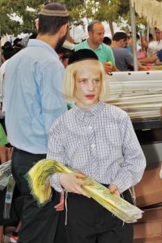 JERUSALEM, ISRAEL - SEPTEMBER 18, 2013: Big market on the eve of the Jewish holiday of Sukkot. The boy - teenager with long blond hair and a black velvet skullcap sells ritual plants