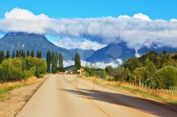 Countryside in Chilean Patagonia. Broad highway leading to the picturesque village. Mountain range is visible in the distance