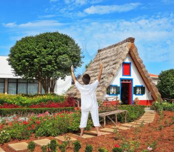 The charming rural lodge with a triangular roof. The slender elderly woman in a white suit for yoga carries out an asana Blessing to the sun.