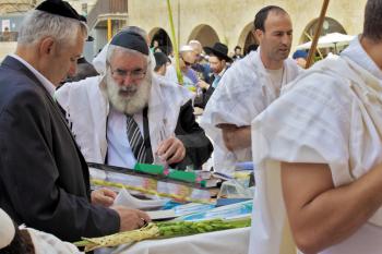 JERUSALEM, ISRAEL - SEPTEMBER 20, 2013:  Prayer at the Kotel. Religious Jews in white prayer shawls are going to pray at the Western Wall of the Temple. Sunny morning in the holiday of Sukkot