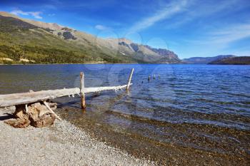 Wooden boat dock on the lake with the cold blue water and pebble beach