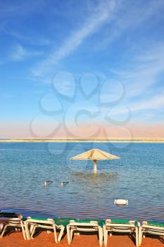 Beautiful sunny day at a beach resort. The Dead Sea, beach umbrellas and deckchairs waiting for tourists