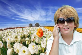 Beautiful blond boy with sunglasses talking on his mobile phone. Behind him, the field of buttercups blooming garden