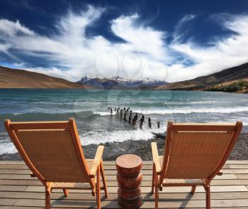 The comfortable place to enjoy the beauty of the lake and clouds in Patagonia. Two folding wooden chairs and a small bedside table on the boardwalk