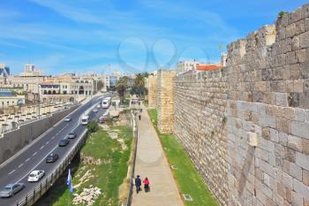 Walk along the walls of ancient Jerusalem. View of the New Jerusalem - the highway with cars, modern buildings and people walking