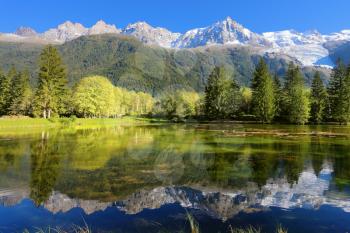Gorgeous reflection in the smooth water of the lake in the park.  Snowy mountains and evergreen forests in the famous mountain resort of Chamonix 