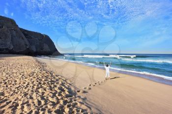 Huge beautiful beach on the Atlantic coast. The seaside resort of Sintra. Middle-aged woman dressed in white doing yoga