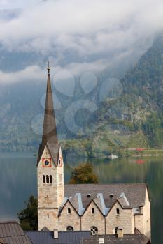 Slender belfry and Lutheran church on the shore of Lake Hallstatt. On the opposite shore of the lake - the beautiful mountains overgrown with forests. The most picturesque small town in Austria - Hall