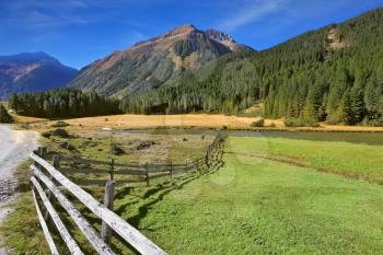 Rural idyll. Headwaters National Park Krimml waterfalls. Farm fields separated from the dirt road the low fence made ​​of logs