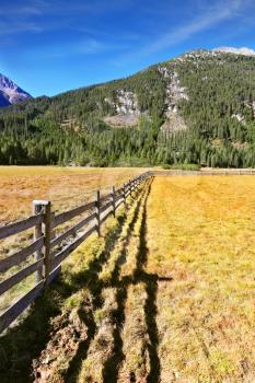 Alpine Valley in Austria. National Park Krimml waterfalls. Scenic farm fields blocked bythe wooden fence. Shadow of the low fence beautifully lie on the grass. 