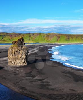 The cape Dirkholaey in the south of Iceland. On beach with black volcanic sand there is a huge rock in the form of a palm