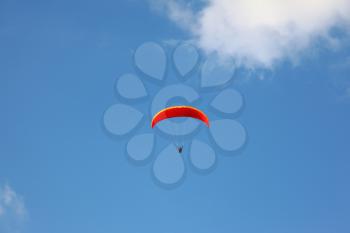 The operated red parachute flies in high in the blue sky