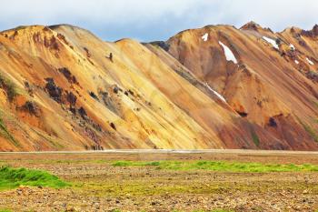 Smooth orange rhyolite mountains in Landmannalaugar nature reserve. In the hollows snow left over from last year