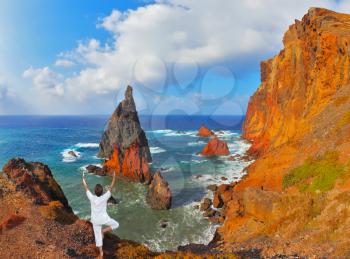 The woman ashore in a white suit for yoga carries out a pose Tree.  Atlantic storms. Colorful pinnacles lit sunset. Arid eastern tip of the island of Madeira