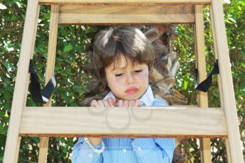 The spoiled beautiful green-eyed boy climbed up a wooden sliding ladder and doesn't want to go down