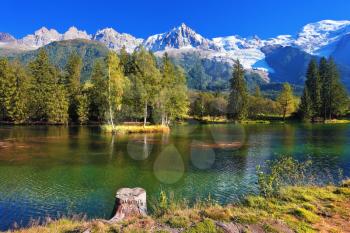  Lake with cold water surrounded by trees and snow-capped mountains. City park in the Alpine resort of Chamonix