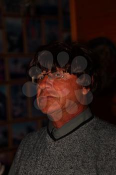 A man with a hard face in the carnival wig and glasses in the darkened interior of the library