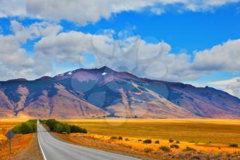 Steppes of Patagonia. Smooth asphalt road passes between the yellow plain to the distant mountains