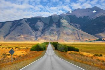  Smooth asphalt road passes between the yellow plains to the distant mountains. Steppes of Patagonia
