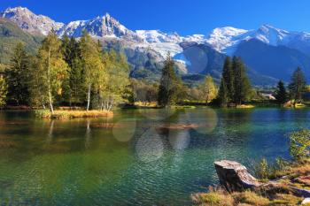  Lake with cold water surrounded by trees and snow-capped mountains. City park in the Alpine resort of Chamonix