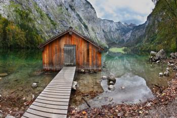 Cloudy day at Lake Koenigssee. Boathouse connected to the coast wooden decking. Clouds and mountains reflected in the water