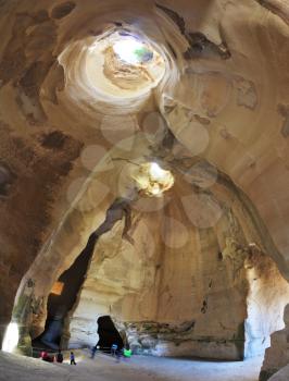 Picturesque clay arches illuminated by the sun from the hole at the top and side entrances. Israel National Park. Bell caves of Beit Guvrin