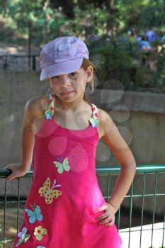 Sweet seven-year-girl in a pink sarafan trimmed appliqus in the form of butterflies, and satin cap