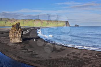 On the beach with black volcanic sand is a huge rock in the shape of palms. Cape Dirholaey in southern Iceland.