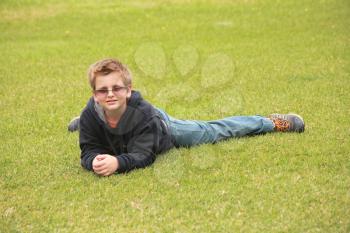 The beautiful boy in solar glasses has a rest on a green lawn in park