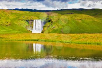 An incredible reflection. Abounding waterfall Skogafoss reflected in  small pond near the road