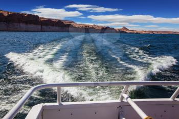  Walk on the tourist boat. Foam boat trail crosses the emerald waters. Red sandstone hills surround the lake Powell on the Colorado River