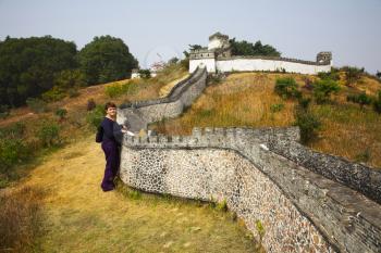 The woman-tourist near to the Great Chinese wall reduced a copy in the Chinese park of entertainments