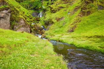 July in Iceland. Picturesque cascade step falls. Basalt mountains overgrown with a green grass and moss