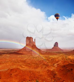 Huge balloon flies over Red Desert Navajo, USA. The picturesque rainbow crosses some rocks - mittens