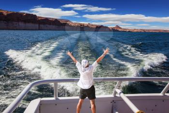 Man in  white shirt on the stern boat fascinated by nature. The lake is surrounded by picturesque beaches of the orange sandstone. Artificial lake Powell on the Colorado River, USA