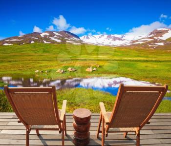 Summer Iceland. Small lake surrounded by green meadow. At the lake on wooden platform there are two deckchairs