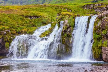 Cloudy day in Iceland. Cascade falls on the green grass mountain